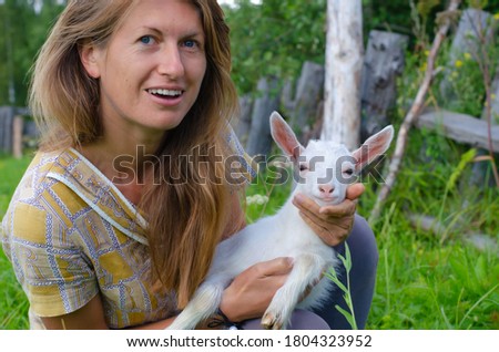 Woman with long hair and a small white kid goat. Countryside, farm, rural concept. People and animals.