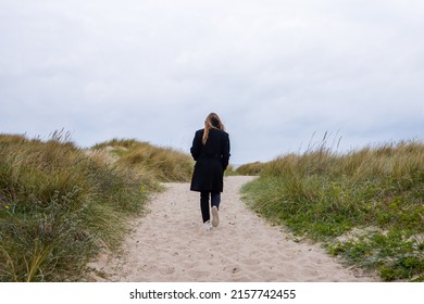Woman with long hair walking in the sand on a path in the dunes near the beach - Shutterstock ID 2157742455