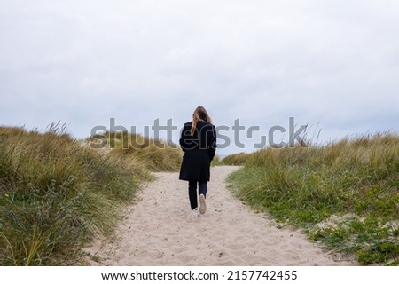 Woman with long hair walking in the sand on a path in the dunes near the beach