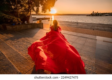 A woman in a long red dress against the backdrop of sunrise, bright golden light of the sun's rays. The concept of femininity, harmony. - Shutterstock ID 2249427475