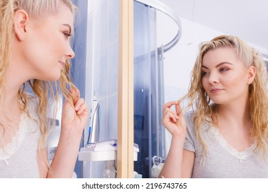 Woman With Long Wet Curly Hair In Bathroom Looking In Mirror. Blonde Girl Taking Care Refreshing Her Hairstyle In Morning. Haircare Concept.