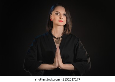 Woman look at camera with zen hands or praying hand symbol on a black background.
