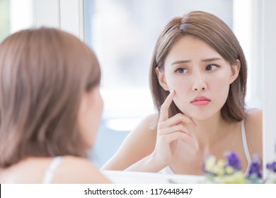 woman look mirrior feel upset and touch her face with acne problem