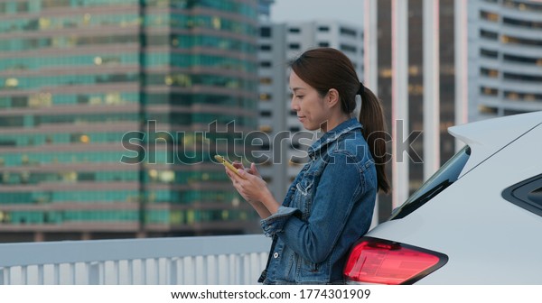 Woman look\
at mobile phone and stand beside her\
car