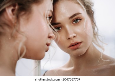 Woman Look at Reflection in Mirror Closeup Photo. Blonde Hair Sensitive Girl Examining Face Beauty Makeup in Bathroom. Serious European Fashionable Lady with Perfect Skin Thinking about Relationship