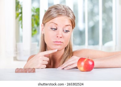 Woman looking at apple and candy, fruit or candy dilemma, healthy lifestyle concept