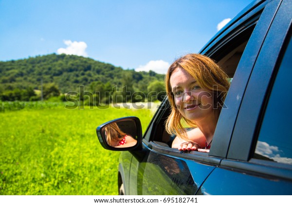 A woman\
looking away from the car window to the mountains in the distance.\
Summer Car trip  travel\
concept.