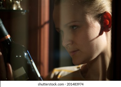 Woman Looking At The Bottle Of Wine Taken From Liquor Cabinet