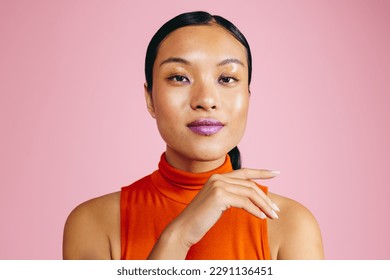 Woman looking at the camera while wearing a bold lip primer, giving her a striking look. Portrait of a woman in her 20s standing in a studio, expressing confidence and assurance in her appearance.