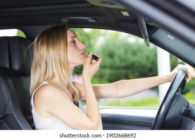 Woman Looking In Car Mirror To Apply Lipstick