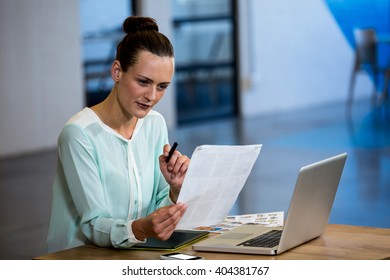 Woman looking a chart with laptop and graphics tablet on desk in office - Shutterstock ID 404381767