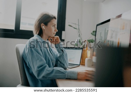 A woman looking at charts and graphs on a computer screen in a bright and sunny coworking space. She appears to be intently focused on the data