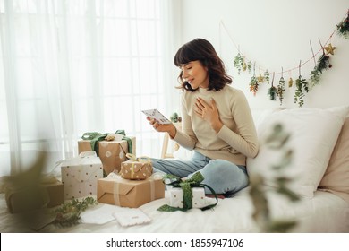 Woman looking at christmas letter. Woman sitting on bed at home with christmas presents and mails.
