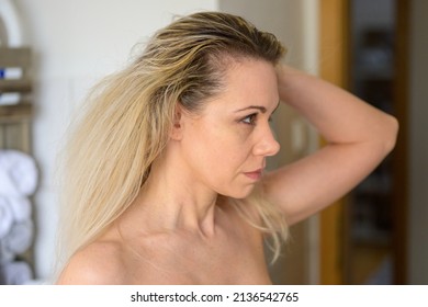 Woman Looking At The Dark Roots If Her Dyed Blond Hair Holding It Back Off Her Forehead In A Close Up Portrait