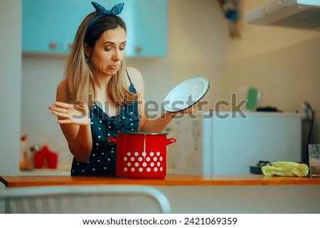 
Woman Looking Disgusted into a Cooking Pot in the Kitchen. Housewife checking the smelly spoiled meal in the soup pot 
