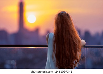 Woman looking and enjoying sunset view from balcony with sun setting behind skyscraper in busy urban downtown with loneliness for solitude, loneliness and dreaming of freedom lifestyle - Powered by Shutterstock