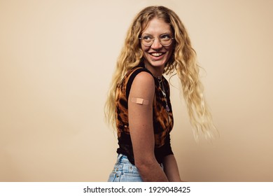 Woman Looking Happy After Getting Vaccine Shot. Caucasian Woman With Bandage On Her Arm After Receiving Vaccination Looking Away On Brown Background.