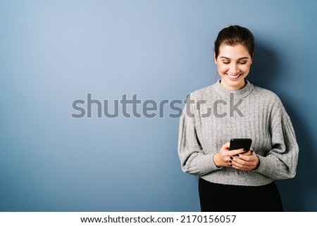 woman looking at her cell phone laughing, copyspace with blue background