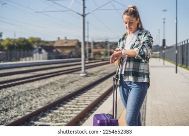 Woman looking at her clock while standing with suitcase  on a train station. - Powered by Shutterstock