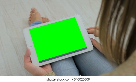 Woman looking at horizontal tablet computer with green screen. Close up shot of woman's hands with pad