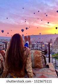 A woman looking at the hot air balloons in Cappadocia at sunrise, from a cave hotel balcony