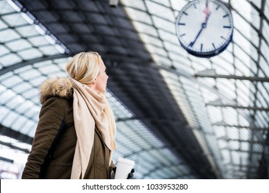 Woman Looking Impassionate At Clock In Train Station As Her Train Has A Delay