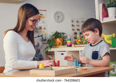 Woman looking at kid playing with didactic colorful toys indoors - preschool