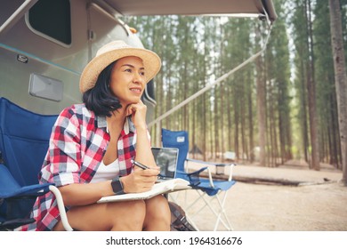 Woman Looking At Laptop Near The Camping. Caravan Car Vacation. Family Vacation Travel, Holiday Trip In Motorhome. Woman Reading A Book Inside The Car Trunk. Female Learning On Travel Break, Laying