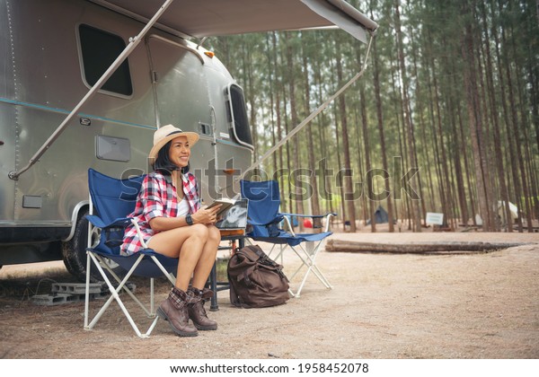 Woman looking at laptop near the camping. caravan\
car vacation. family vacation travel, holiday trip in motorhome.\
woman reading a book inside the car trunk. female learning on\
travel break, laying