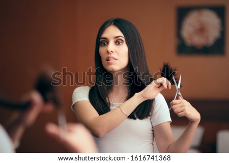 
Woman Looking in Mirror Cutting Split Hair Ends. Girl changing looks giving herself a with DIY cut 
