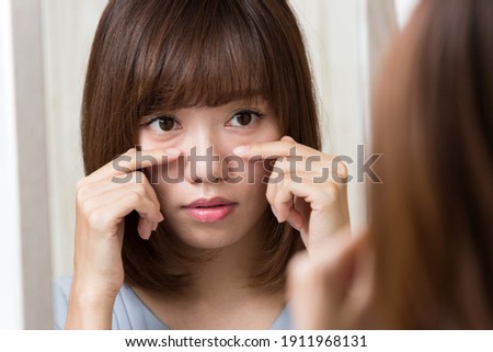 The woman is looking in the mirror and touching her lower eyelids. [[stock_photo]] © 