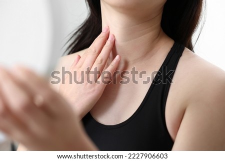 A woman looking in the mirror while touching her neck wrinkles