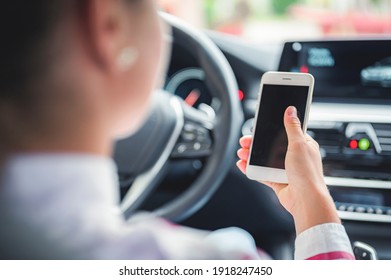 Woman Looking At Mobile Phone While Driving A Car. Driver Using Smart Phone In Car