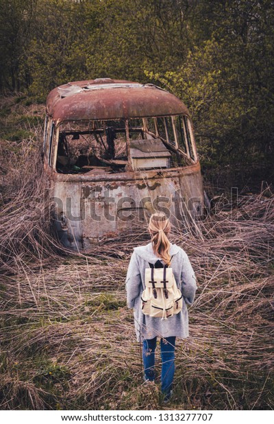 Woman looking to old rusty bus in rural\
scenery. People and environment. Waste in\
nature