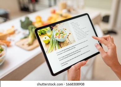 Woman looking on the digital recipe, using touchscreen tablet while cooking healthy meal on the kitchen at home, close-up view on the screen - Shutterstock ID 1668308908