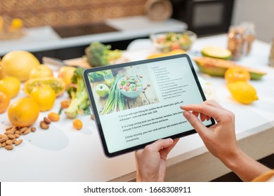 Woman looking on the digital recipe, using touchscreen tablet while cooking healthy meal on the kitchen at home, close-up view on the screen - Shutterstock ID 1668308911