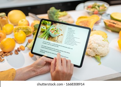 Woman looking on the digital recipe, using touchscreen tablet while cooking healthy meal on the kitchen at home, close-up view on the screen