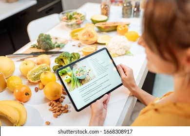 Woman looking on the digital recipe, using touchscreen tablet while cooking healthy meal on the kitchen at home, close-up view on the screen - Shutterstock ID 1668308917