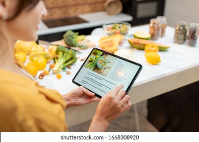 Woman looking on the digital recipe, using touchscreen tablet while cooking healthy meal on the kitchen at home, close-up view on the screen - Shutterstock ID 1668308920