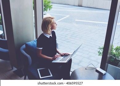 Woman Is Looking On Street Outside The Window, While Is Sitting With Net-book And Touch Pad In Luxury Restaurant. Young Female Is Thinking About Something After Learning On-line Via Laptop Computer