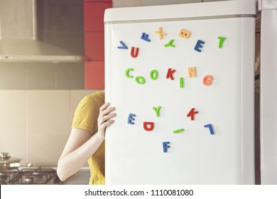 Woman looking in open fridge with Cooking  letters on door. Cooking for family and children concept