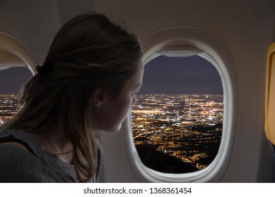 Woman looking out of the plane from the window during a night flight. City lights view