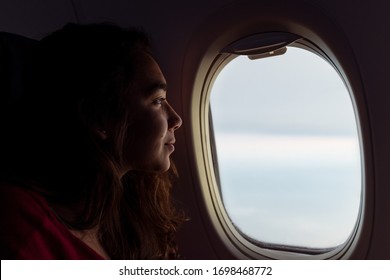 Woman Looking Out Of The Window On Aeroplane In Flight With Clouds Sky Visible Through Window. Dark Photo Of Woman Looking Out Of Plane Window. AUSTRALIA. March, 2020.