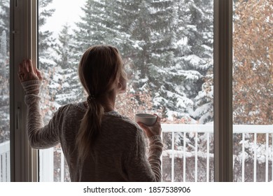 Woman Looking Out Window In Winter Holding Coffee In Hand