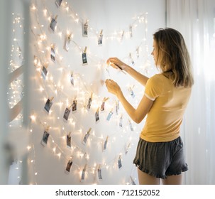Woman Looking At Photos Hanging With Decoration Lights On The White Wall
