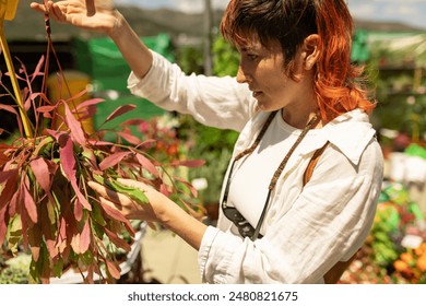 A woman is looking at a plant in a greenhouse. She is wearing a white shirt and a red headband - Powered by Shutterstock