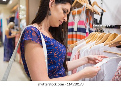 Woman Looking At Price Tag Of Clothes In Shopping Mall