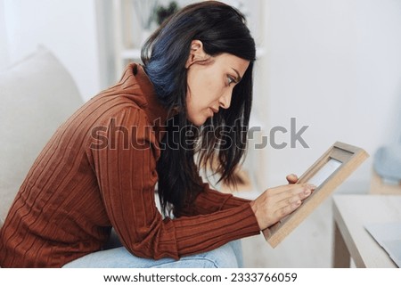 Woman looking sadly at the picture frames in her hands, crying over memories, state of depression and loss of a person