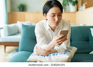 Woman looking at smartphone in living room - Shutterstock ID 2140241191