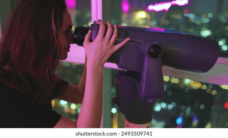 Woman looking in telescope at night city. Tourist enjoys Bangkok Baiyoke Tower Sky viewpoint. Colorful cityscape center downtown, night lights view from top floor. Travel, tourism - Powered by Shutterstock